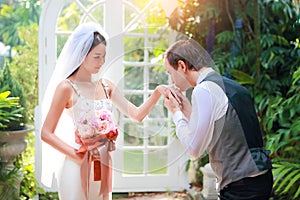 Handsome caucasian groom is holding and kissing asian bride hand with love and smiling face during wedding or pre wedding photo