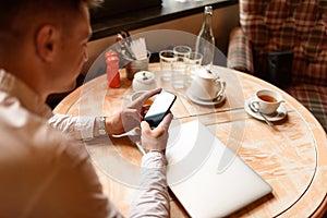 Handsome Caucasian guy using smartphone in cafe