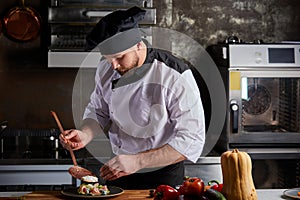 Handsome caucasian male chef adding piquancy to dish photo