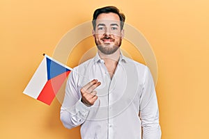 Handsome caucasian man with beard holding czech republic flag looking positive and happy standing and smiling with a confident