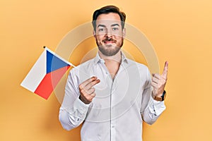 Handsome caucasian man with beard holding czech republic flag smiling happy pointing with hand and finger to the side