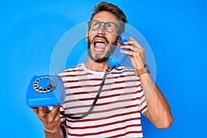 Handsome caucasian man with beard holding vintage telephone angry and mad screaming frustrated and furious, shouting with anger