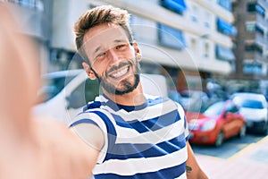 Handsome caucasian man with beard smiling happy taking a selfie picture outdoors