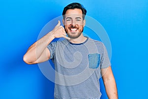 Handsome caucasian man with beard wearing casual striped t shirt smiling doing phone gesture with hand and fingers like talking on