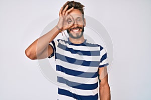 Handsome caucasian man with beard wearing casual striped t-shirt smiling happy doing ok sign with hand on eye looking through