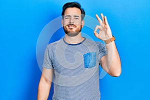 Handsome caucasian man with beard wearing casual striped t shirt smiling positive doing ok sign with hand and fingers
