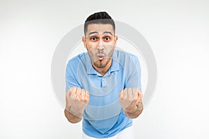 Handsome caucasian man in a blue t-shirt holds fists for good luck on a white studio background