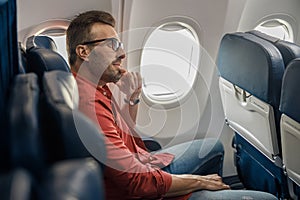 Handsome caucasian man in casual wear and glasses looking away, sitting on the plane near the window