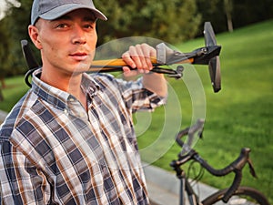 Handsome caucasian man in casual wear looking at camera, holding bicycle pump for inflating the tire of his bike