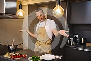 Handsome Caucasian man in chef's apron cooking family dinner, smiling looking at camera