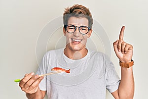 Handsome caucasian man eating prawn sushi using chopsticks smiling happy pointing with hand and finger to the side