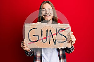 Handsome caucasian man with long hair holding no guns warning banner smiling with a happy and cool smile on face