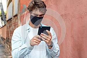 Handsome caucasian man reading an ebook on the street and wearing a mask. New normality concept