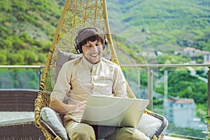 Handsome caucasian man sitting on the terrace working from home using computer laptop. Young man teaches a foreign