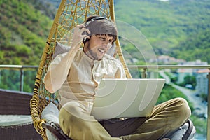 Handsome caucasian man sitting on the terrace working from home using computer laptop. Young man teaches a foreign