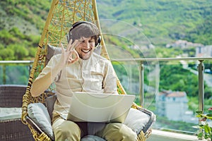 Handsome caucasian man sitting on the terrace working from home using computer laptop. Young man teaches a foreign