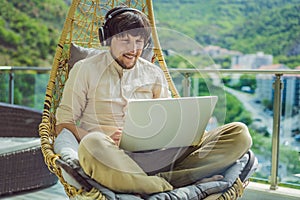 Handsome caucasian man sitting on the terrace working from home using computer laptop. Young man teaches a foreign