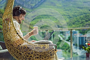 Handsome caucasian man sitting on the terrace working from home using computer laptop. Young man teaches a foreign