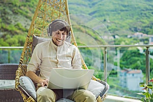 Handsome caucasian man sitting on the terrace working from home using computer laptop. Young man teaches a foreign