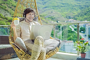 Handsome caucasian man sitting on the terrace working from home using computer laptop. Young man teaches a foreign