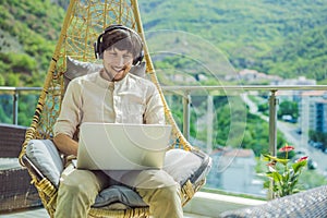 Handsome caucasian man sitting on the terrace working from home using computer laptop. Young man teaches a foreign