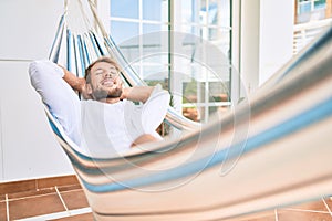 Handsome caucasian man smiling happy resting on a hammock at the terrace