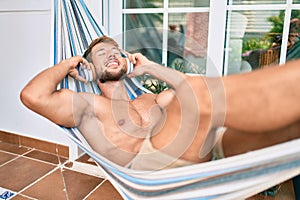 Handsome caucasian man smiling happy resting on a hammock at the terrace listening to music wearing headphones