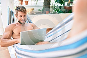 Handsome caucasian man smiling happy resting on a hammock at the terrace using computer laptop
