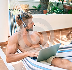 Handsome caucasian man smiling happy resting on a hammock at the terrace working from home wearing call center headset