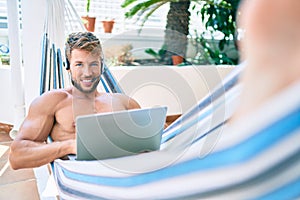 Handsome caucasian man smiling happy resting on a hammock at the terrace working from home wearing call center headset