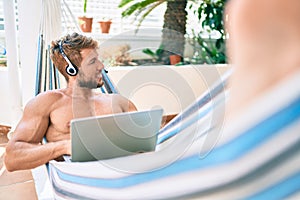 Handsome caucasian man smiling happy resting on a hammock at the terrace working from home wearing call center headset