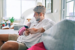 Handsome caucasian man smiling happy sitting on the sofa at home using smartphone