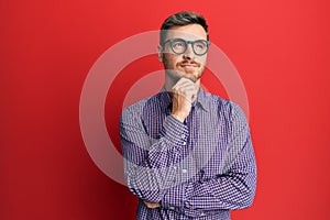 Handsome caucasian man wearing business shirt and glasses thinking concentrated about doubt with finger on chin and looking up