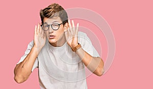 Handsome caucasian man wearing casual clothes and glasses trying to hear both hands on ear gesture, curious for gossip
