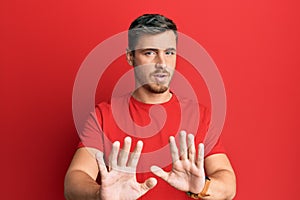 Handsome caucasian man wearing casual red tshirt moving away hands palms showing refusal and denial with afraid and disgusting
