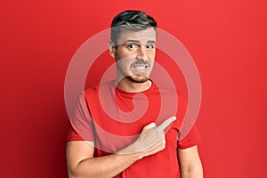 Handsome caucasian man wearing casual red tshirt pointing aside worried and nervous with forefinger, concerned and surprised