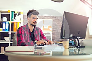 Handsome caucasian man at work desk facing flat screen computer