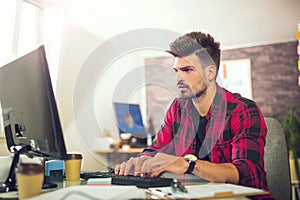 Handsome caucasian man at work desk facing flat screen computer