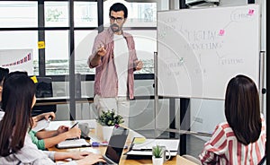 Handsome Caucasian smart casual businessman presenting, pointing at marketing financial graph or chart on whiteboard to his