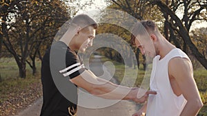 Handsome Caucasian sportsmen standing in sunlight in the autumn park boasting their muscles and laughing. Two young