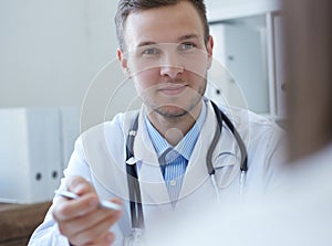 Handsome Caucasian young male doctor talking to patient at office. Healthcare and medical concept.