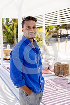 Handsome caucasian young man with hands in pockets smiling and standing at tourist resort