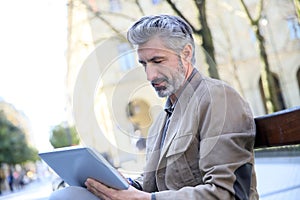 Handsome charming man websurfing on tablet in the streets