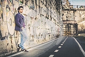 Handsome and charming young man outdoors leans against a wall in the city