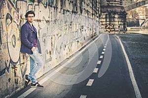 Handsome and charming young man outdoors leans against a wall in the city