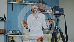 Handsome cheerful man recording video food blog about cooking on dslr camera in kitchen at home