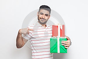 Handsome cheerful positive young bearded man looking at camera, pointing at two gift boxes.