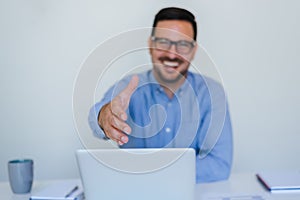 Handsome cheerful smiling young businessman entrepreneur manager or business partner offering hand for handshake in office gives