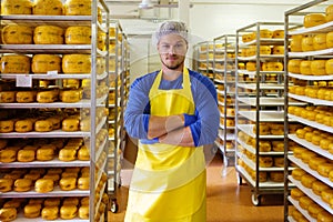 Handsome cheesemaker is checking cheeses in his workshop storage.