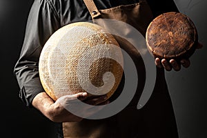 Handsome cheesemaker is checking cheeses in his workshop storage, close up